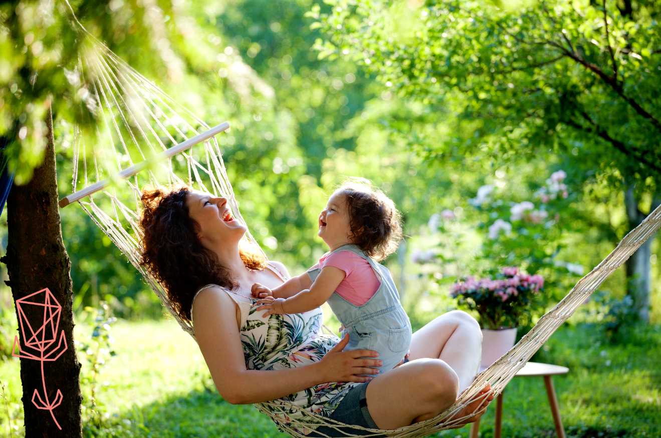 Mom and baby sitting in a hammock and laughing with green garden in background